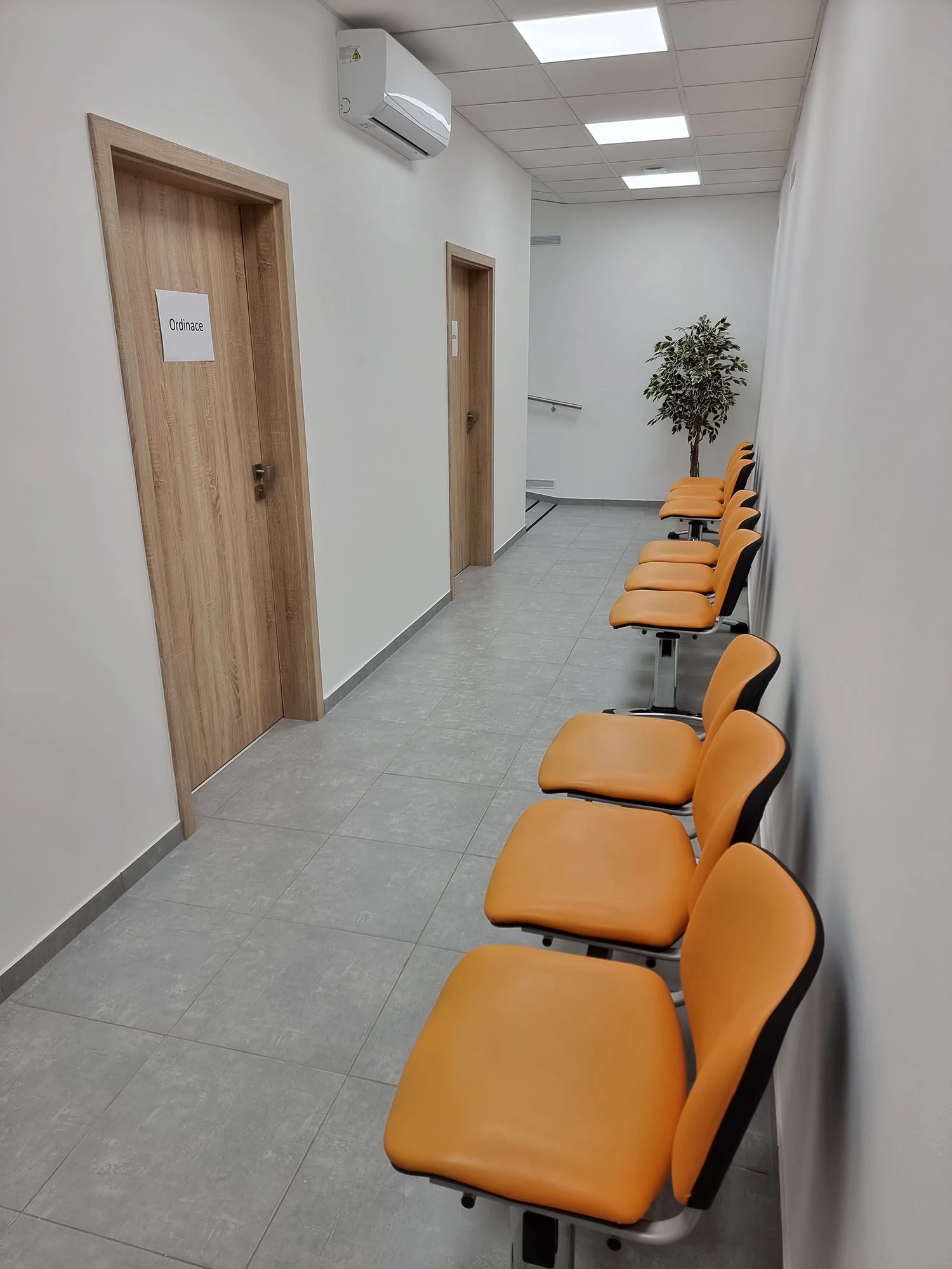 Čekárna s oranžovými židlemi a dveřmi do ordinace